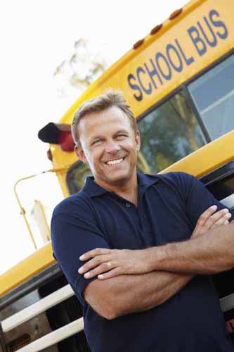 A school bus driver stands in front of a school bus.